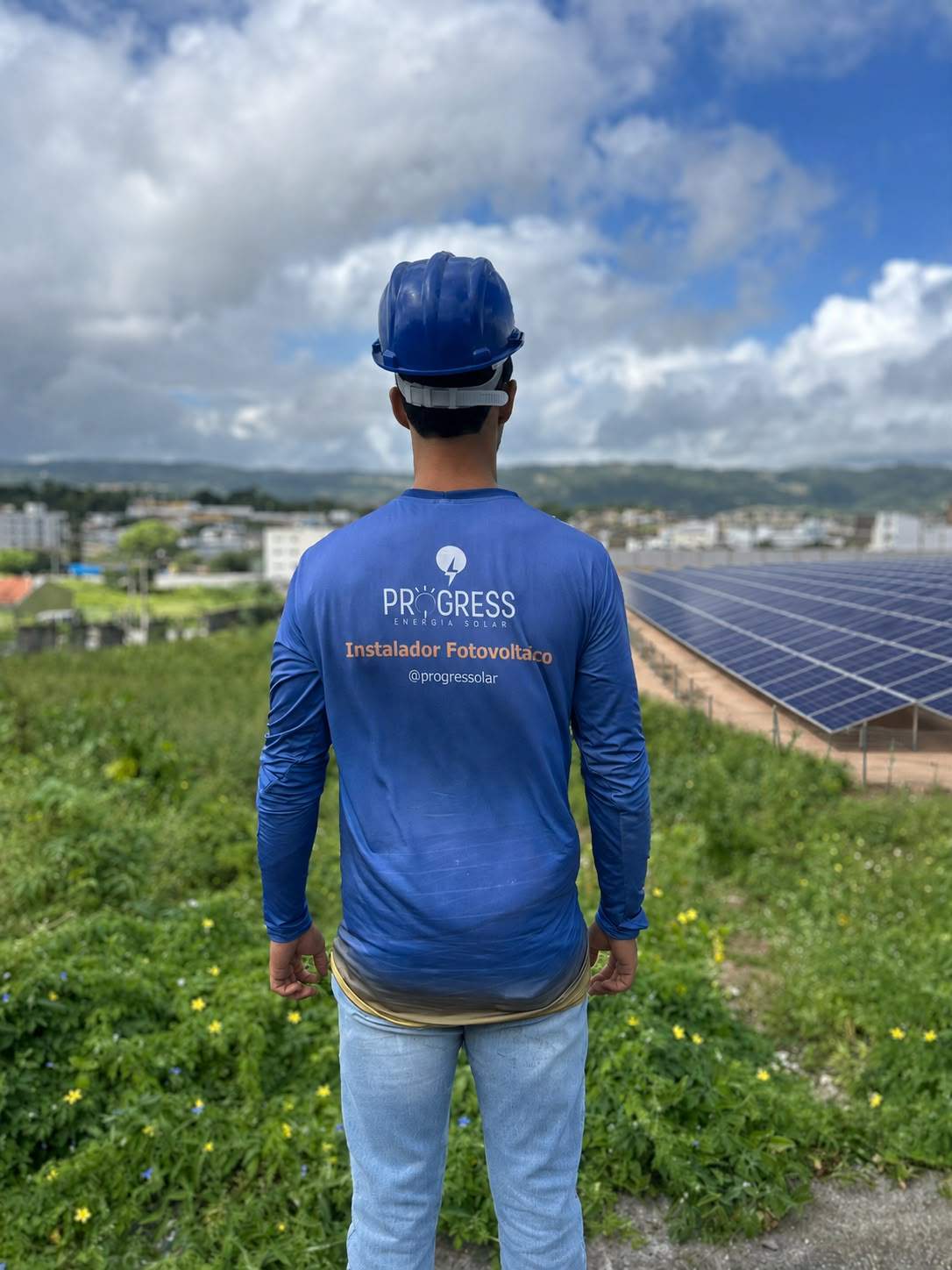 Integrante da Progress com uniforme e capacete diante de uma instalação solar